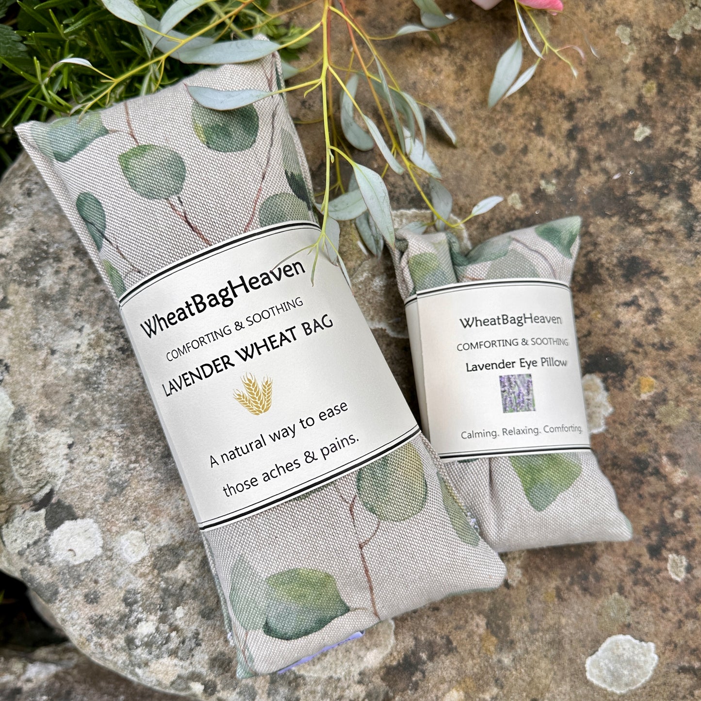 Lovely lavender scented wheat bag heat wrap next to a flax seed filled eye pillow in the same botanical print, eucalyptus leaves on a beige background. Pictured in the garden of wheat bag heaven
