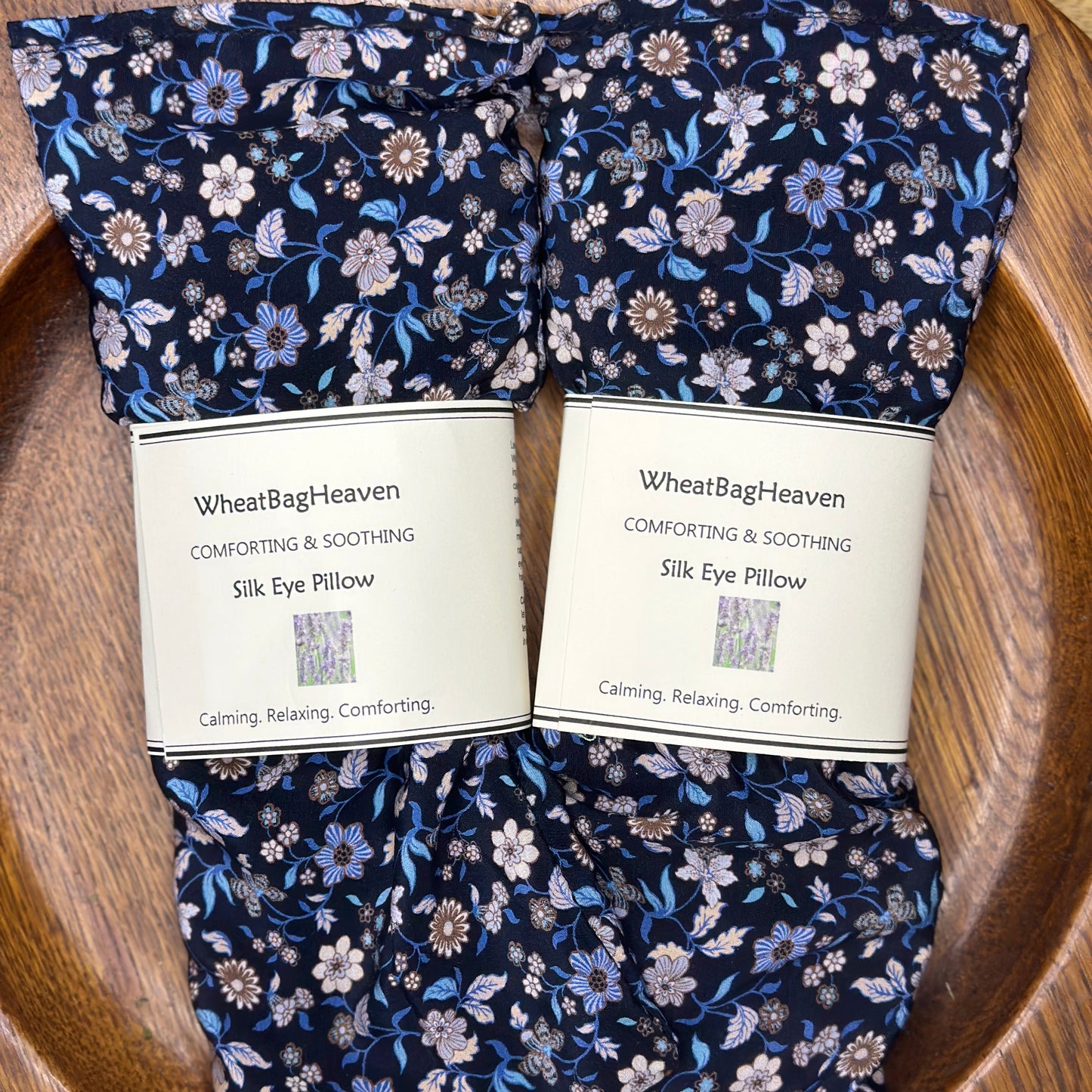 A pair of Liberty silk eye pillows in blue floral print on a wooden tray