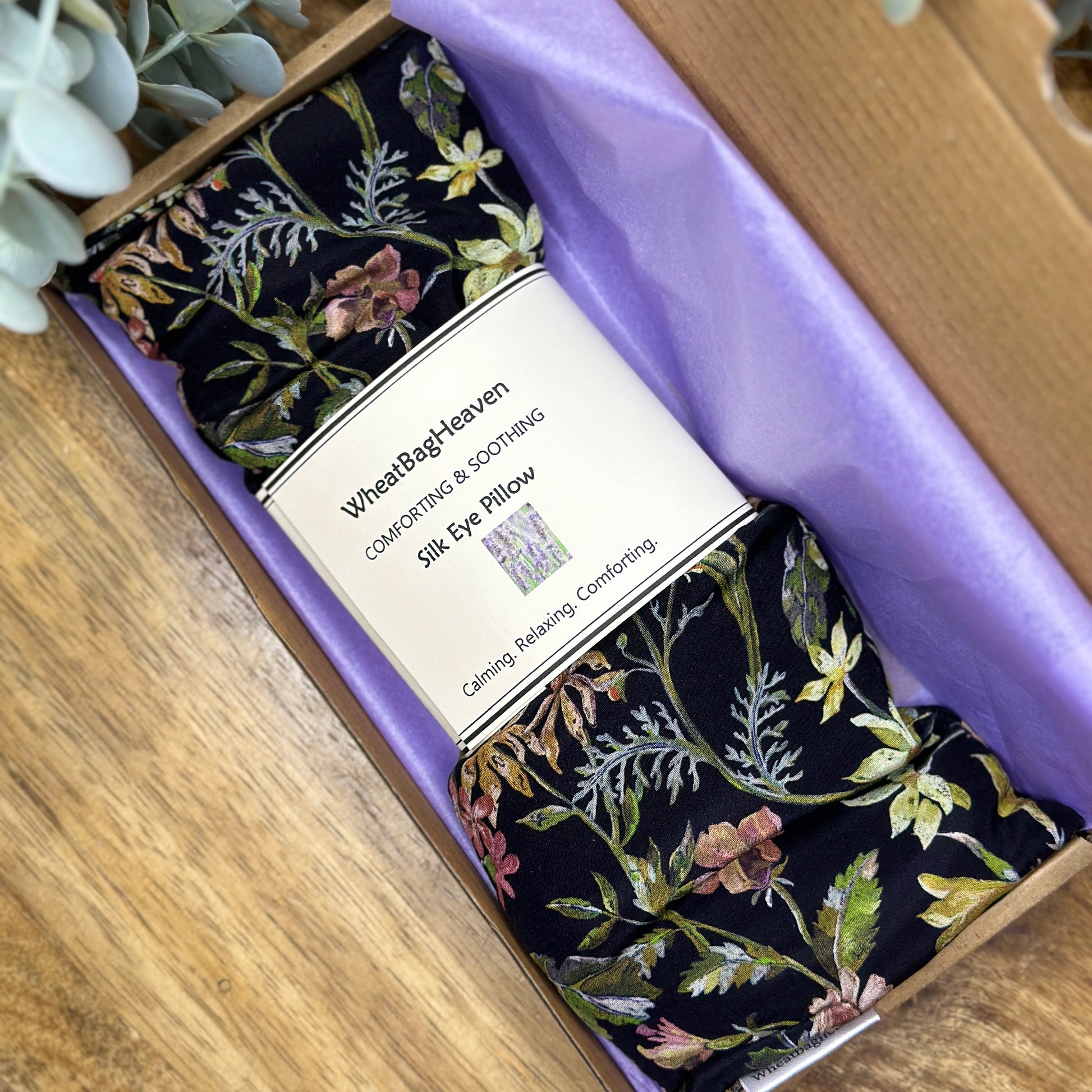 Ready to gift silk floral eye pillow laid on lilac tissue paper in a gift box on wooden table