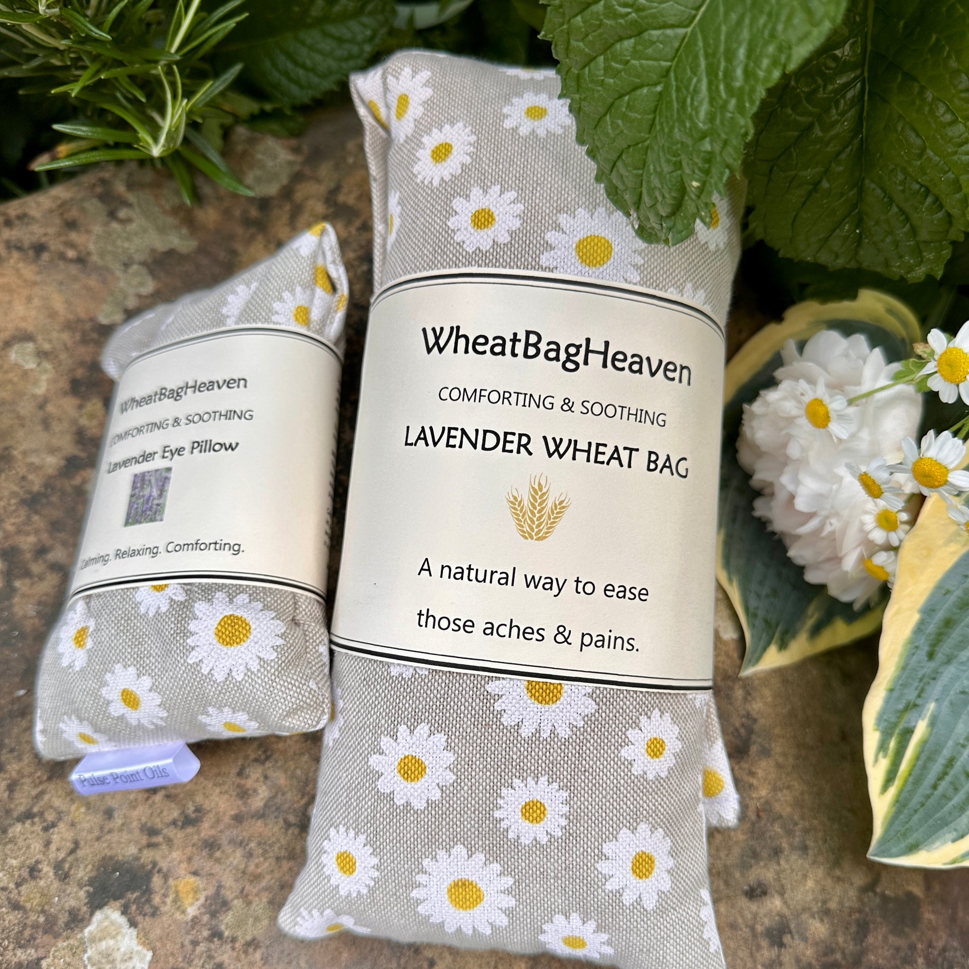 Lavender scented long cotton wheat bag with a matching eye pillow to soothe and comfort, surrounded by rosemary, mint, daisies, hostas in the garden of WheatBagHeaven 