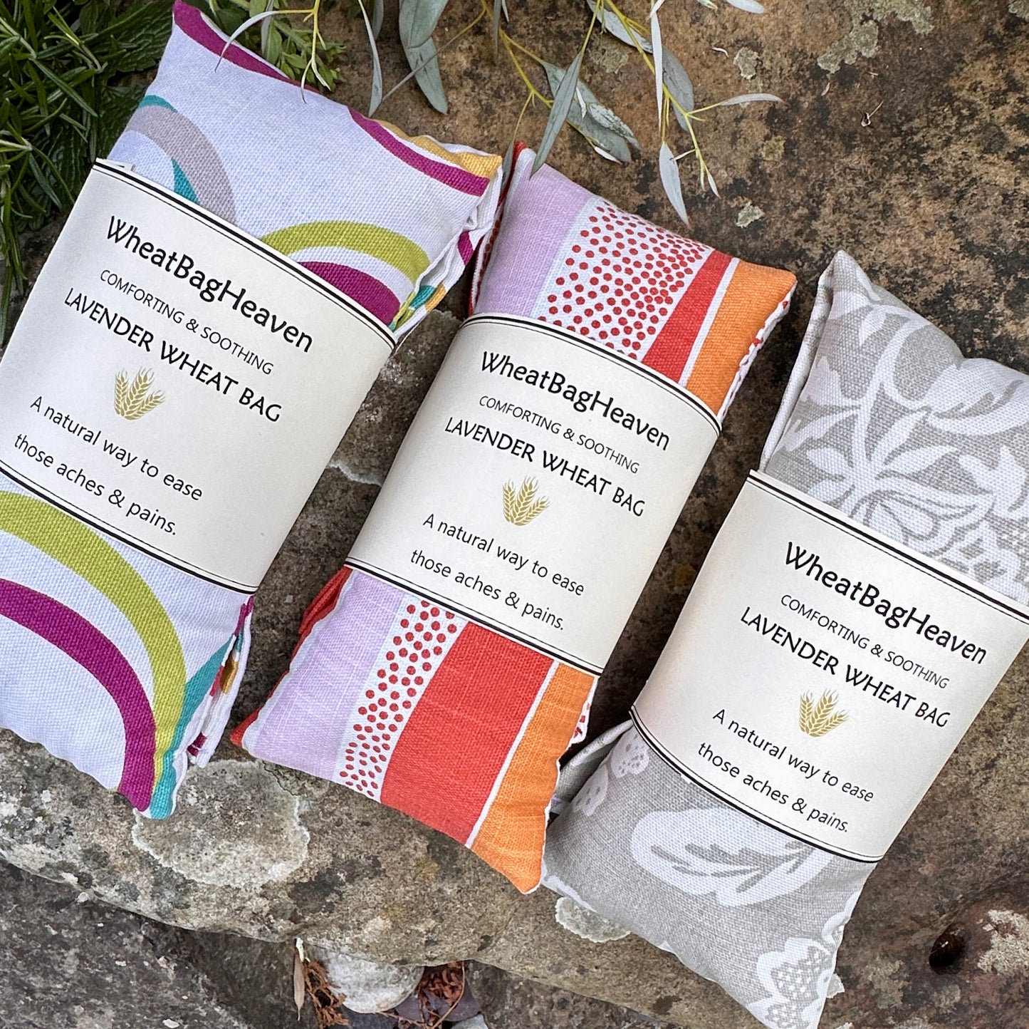 Three lavender scented wheat bags in the garden of WheatBagHeaven. From left to right cotton prints we have coloured circles on light background, heat wrap, zesty orange and beige seedhead print