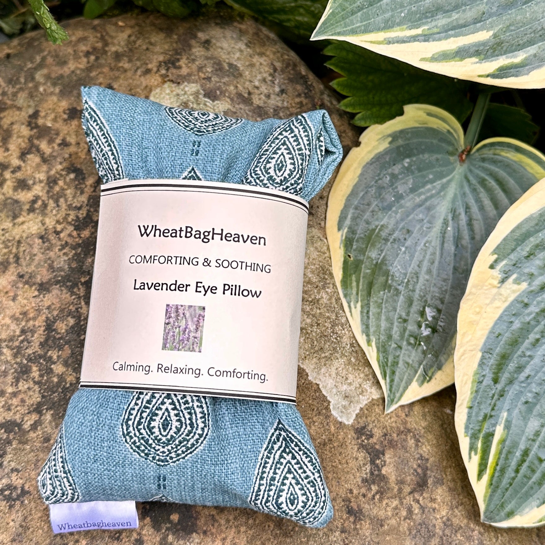 lavender scented eye pillow in a teal blue cotton fabric, folded in half with WheatBagHeaven belly band. 