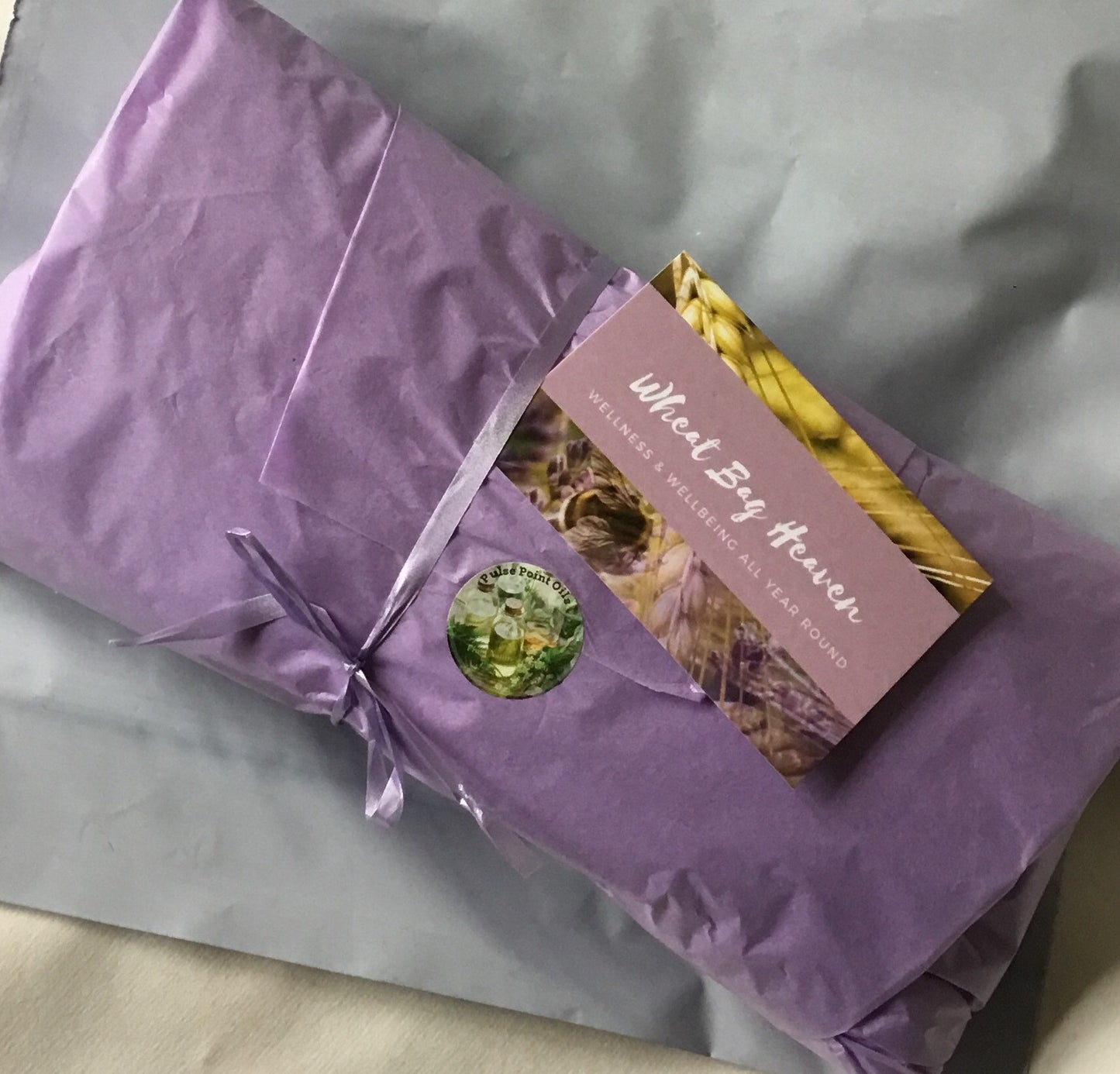 wheat bag wrapped in lilac tissue paper and tied with ribbon on a grey postal bag