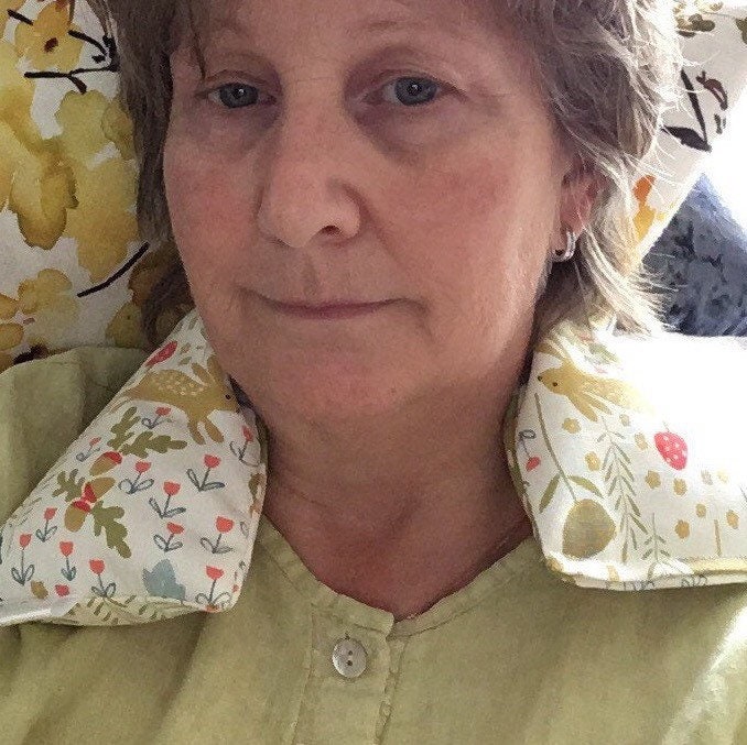 Female sat relaxing with a lavender scented wheat bag neck wrap from WheatBagHeaven. The wheat bag is woodland animals in a scandi cotton print on light background