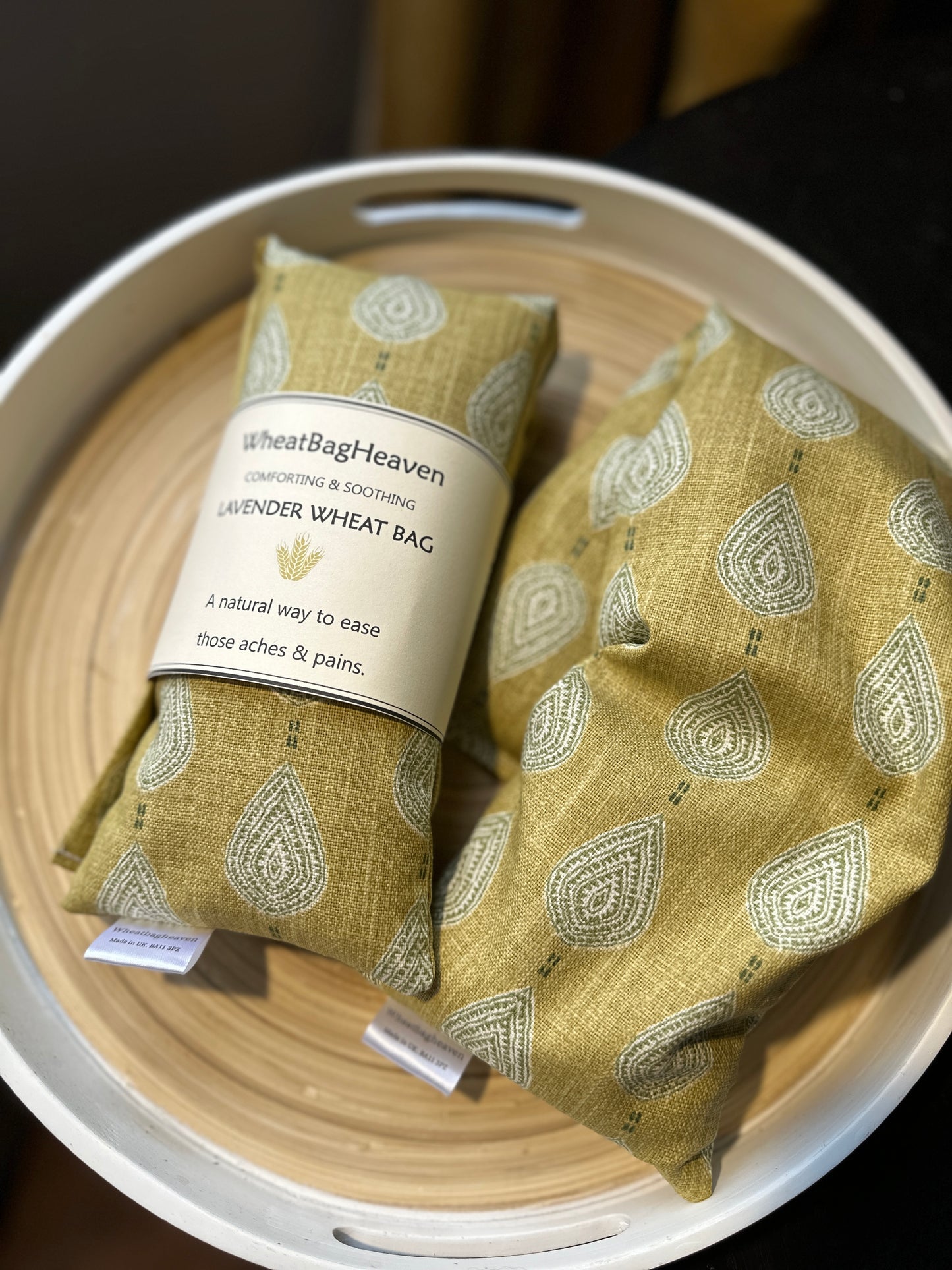 two paisley teardrop ochre wheat bag with lavender scent, one wheat bag is labelled 'WheatBagHeaven' comforting and soothing lavender wheat bag. A natural way to ease those aches and pains. Has a makers tag which reads WheatBagHeaven