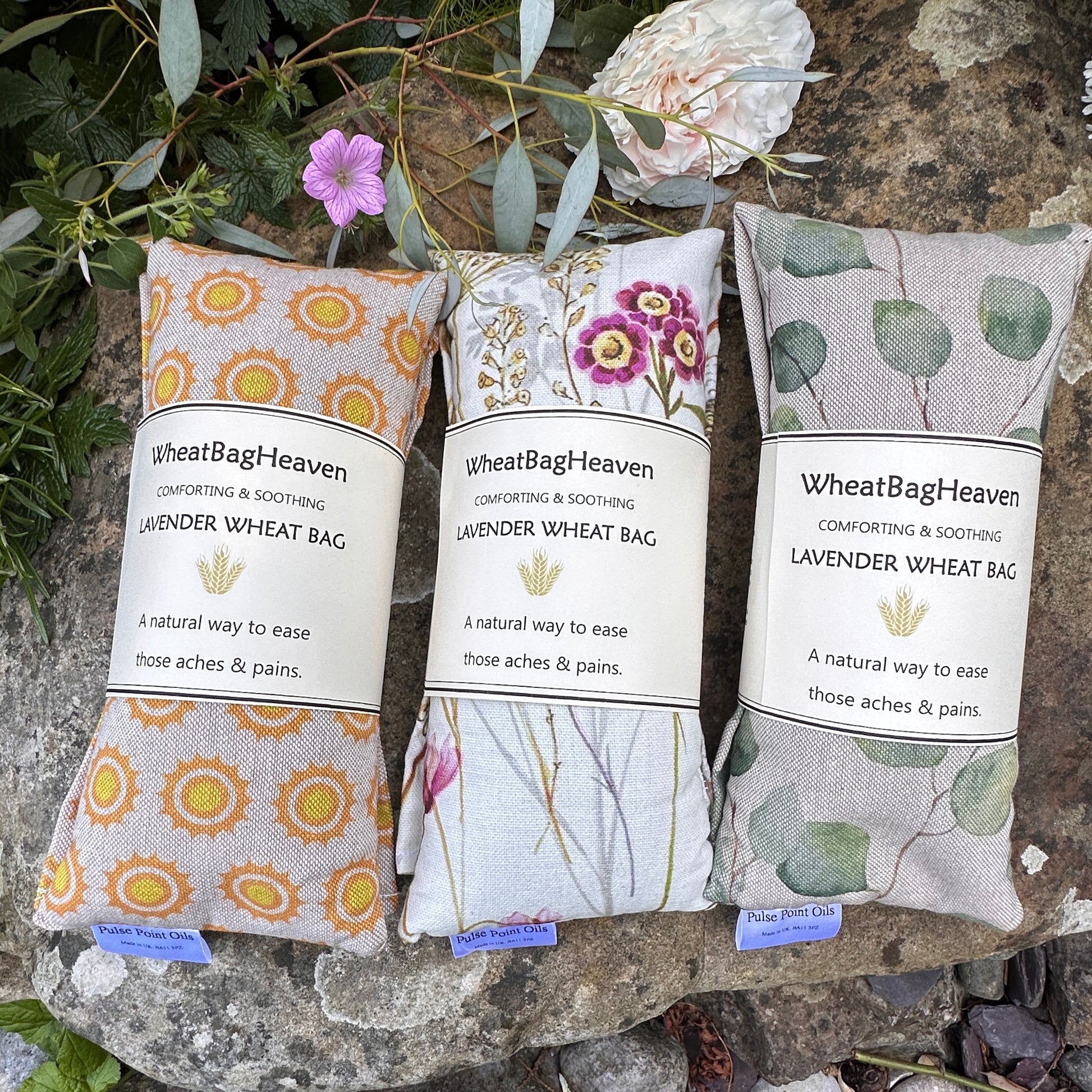 Three lavender scented wheat bags in the gardens of WheatBagHeaven. From left to right all on cotton linen fabric, sunshine print, wetlands habitat print and then beautiful eucalyptus leaf print on a beige background. Size 47x12cm