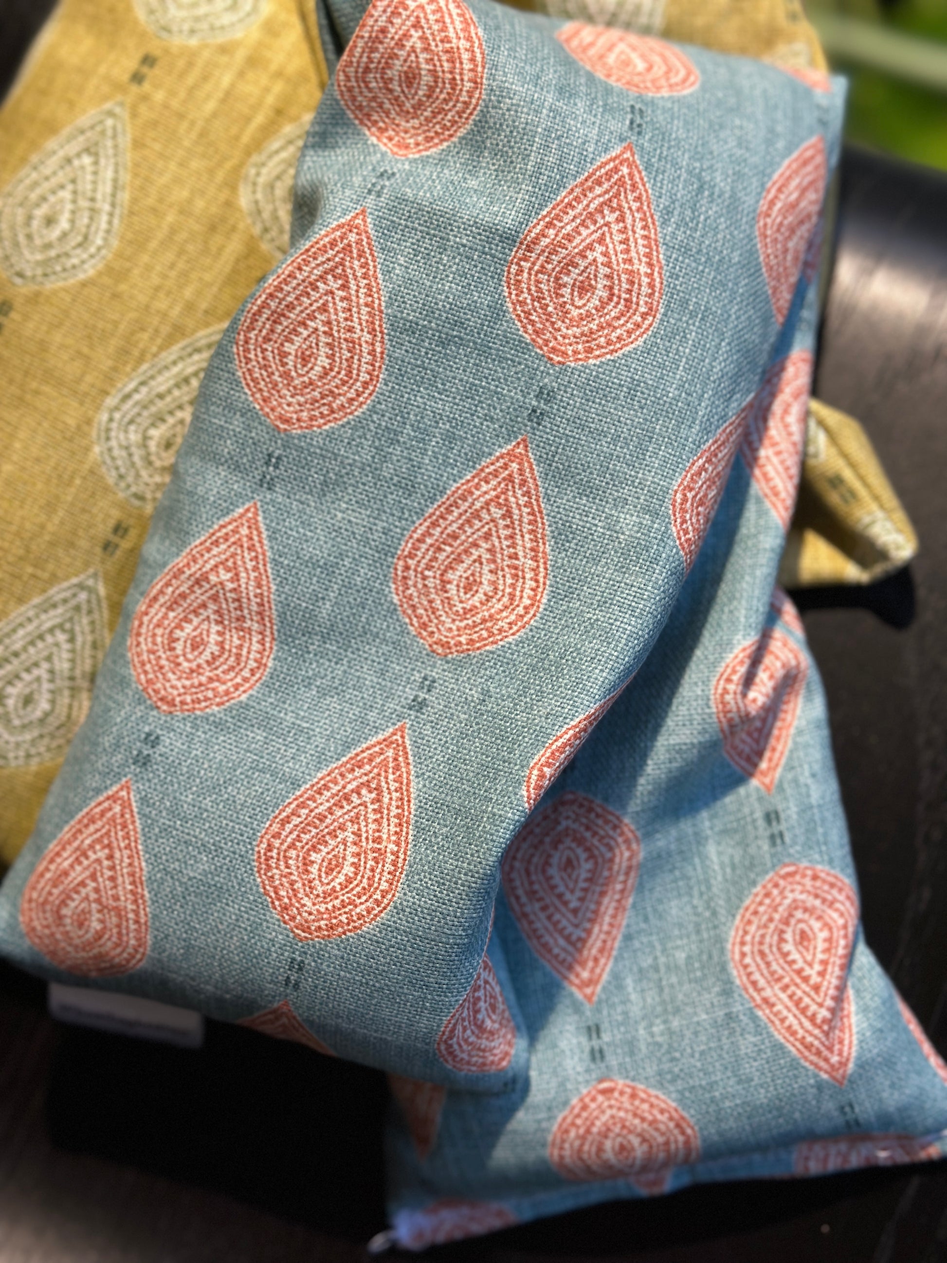 Lavender wheat bag on a black background with close up of the soft teal blue fabric with pink paisley teardrop pattern 