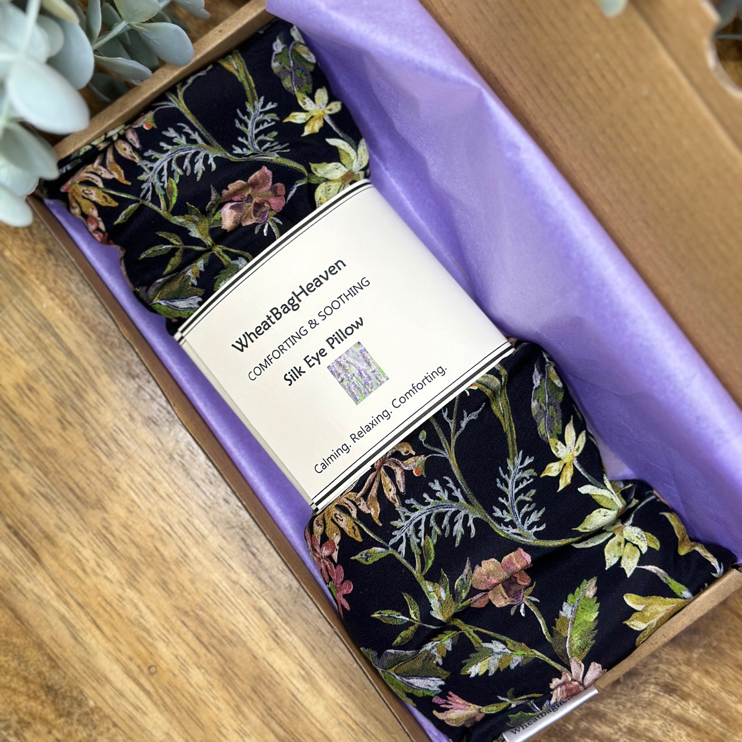 Ready to gift silk floral eye pillow laid on lilac tissue paper in a gift box on wooden table 