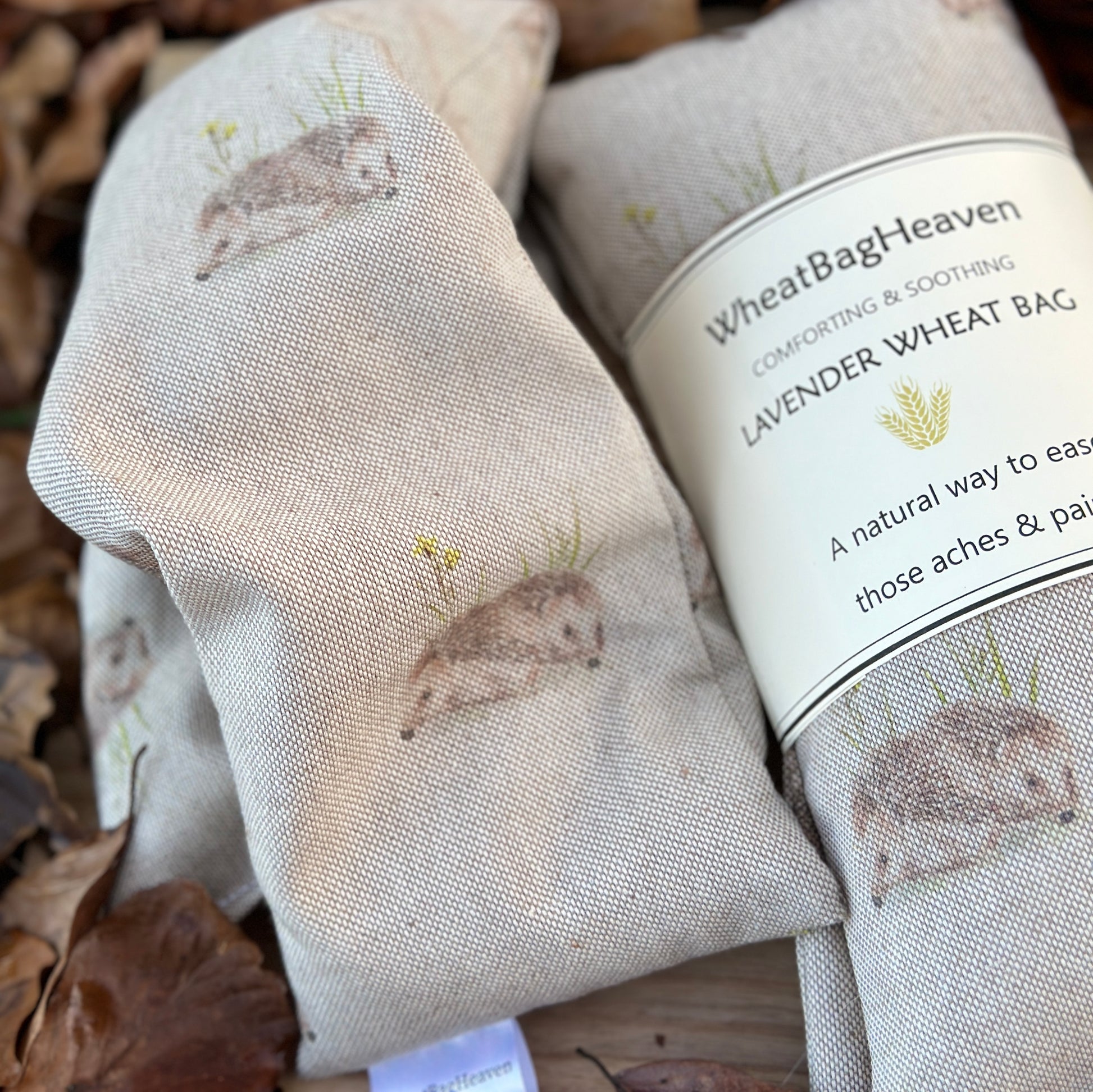 Close up shot of two wheat bags with Somerset whole wheat and lavender, the cotton fabric print is of  brown hedgehog pairs amongst grass on a beige background 