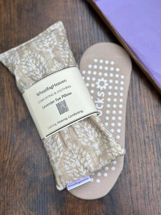 Eye pillow in cream and beige botanical print along side beige yoga socks with packaging on a wooden surface