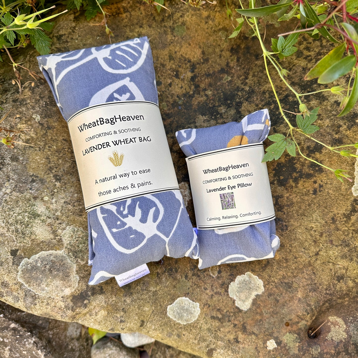denim blue background with white leaf and yellow berry print. wheat bag and eye pillow combination for self care and wellbeing. handmade by wheat bag heaven and pictured on a rock side by side