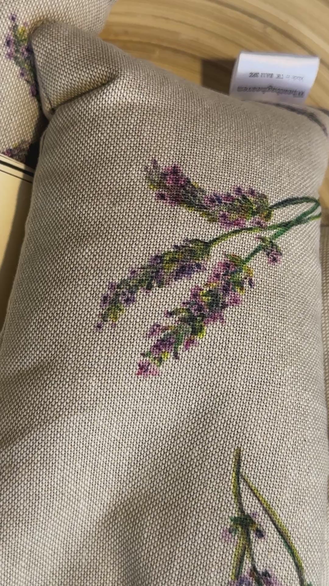 short video of Two Wheat bags with a lavender flower print design on a wooden surface. One wheat bag has maker's belly band that read WheatBagHeaven comforting and soothing Lavender Wheat Bag A natural way to ease those aches and pains. Both have makers tags