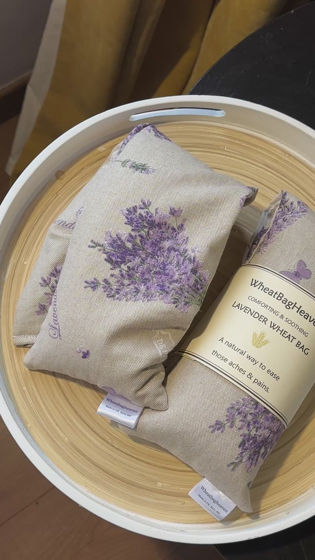 a short video of Two Wheat bag with lavender floral bouquet print and label that reads WheatBagHeaven comforting and soothing Lavender Wheat Bag. A natural way to ease those aches and pains. The wheat bags are laid in a wooden tray